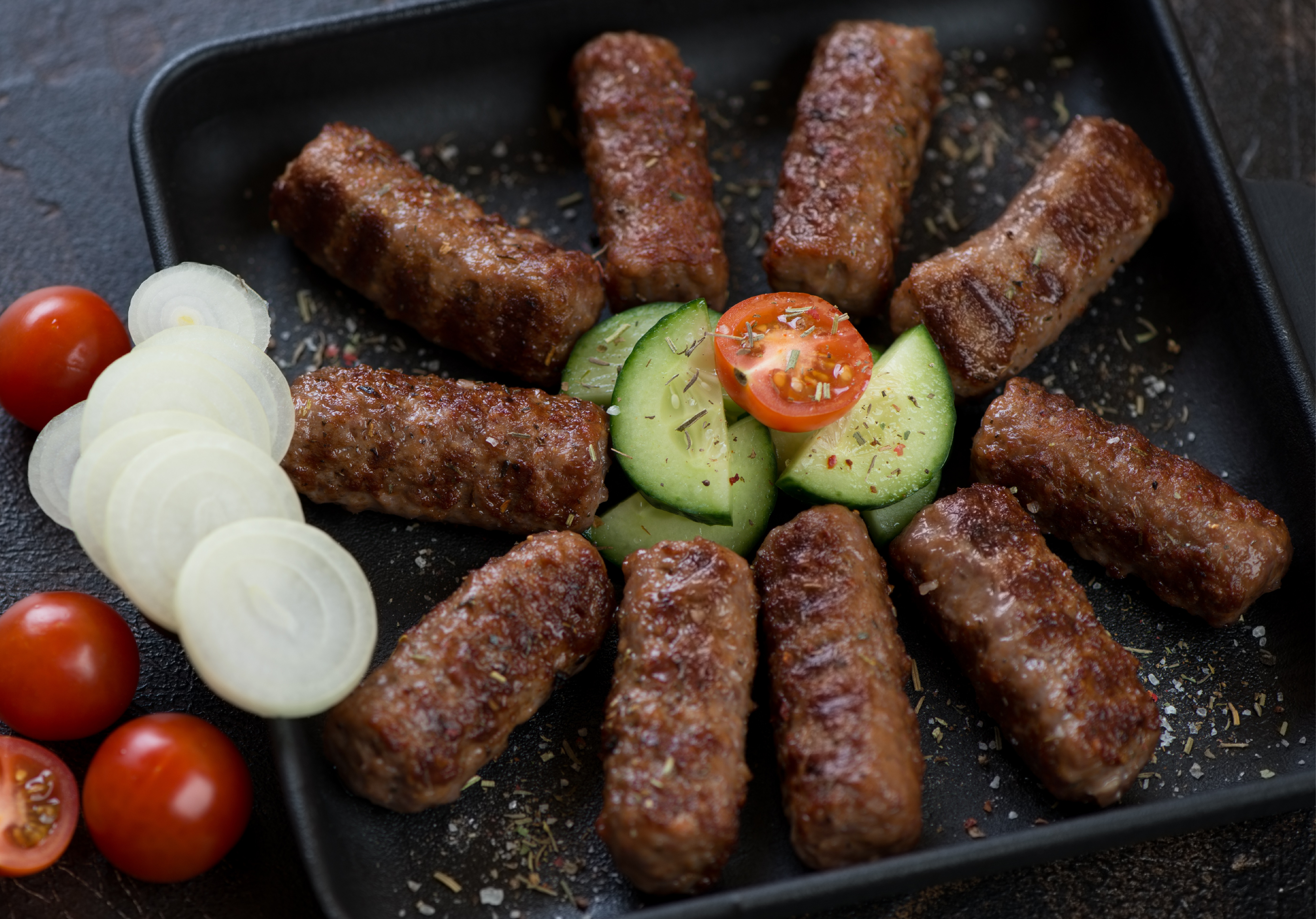 Grilled Cevapi seasoned with herbal spices and served with fresh cucumber, tomatoes and onions. 