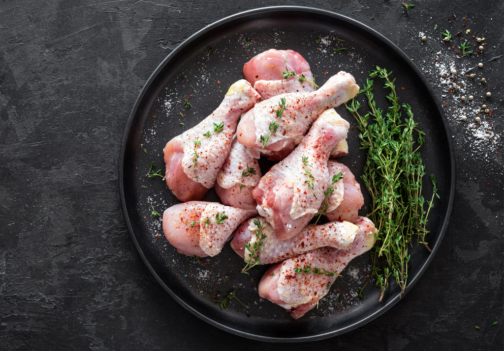 Raw chicken drumsticks seasoned with paprika and thyme leaves. Dish garnished with sea salt and peppercorns. King George's Steak and Seafood.