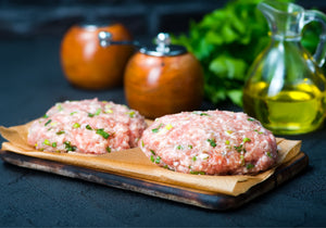 Raw chicken burgers displayed on top of a wooden cutting board. King George's Steak and Seafood. 