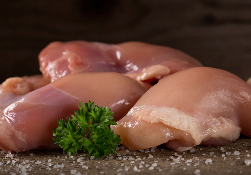 Raw chicken thighs displayed on top of a sea salt layer and parsley. King George's Steak and Seafood.