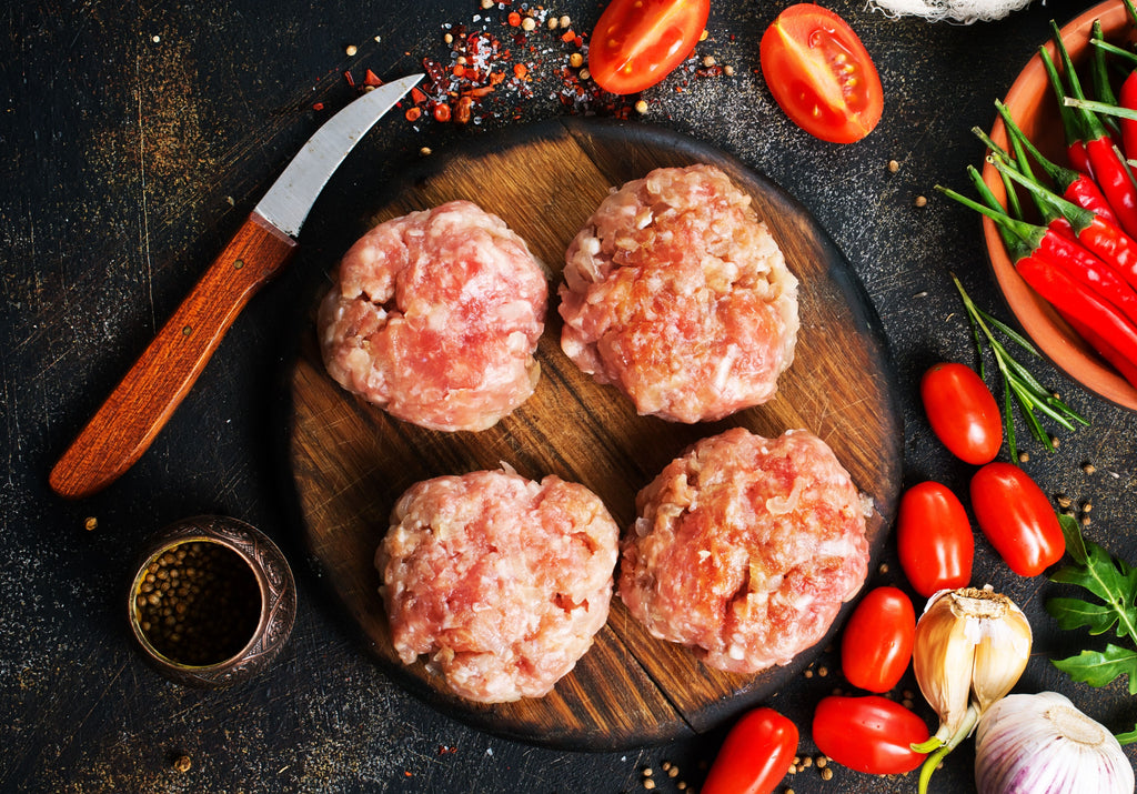 Raw Ground Chicken formed into round patties; displayed with cherry tomatoes, peppercorn, red chilies, garlic and other spices. King George's Steak and Seafood.