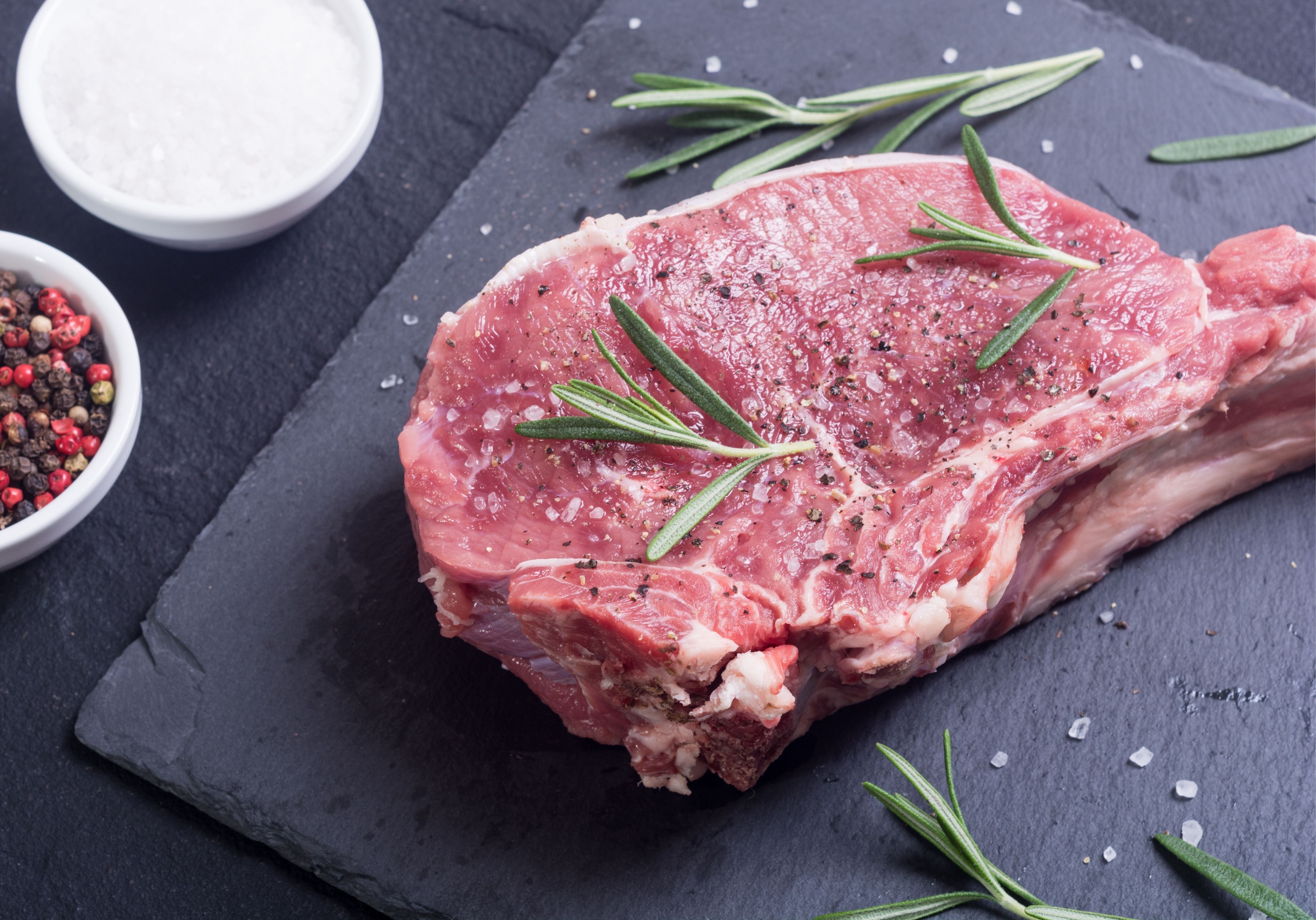 Raw Prime Rib Steak displayed with peppercorn, sea salt, and rosemary. King George's Steaks and Seafood.