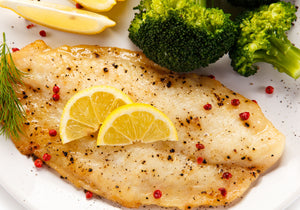 Baked Tilapia fillet seasoned with pepper and garnished with lemon wheels, fresh rosemary, and served with broccoli. King George's Steak and Seafood.