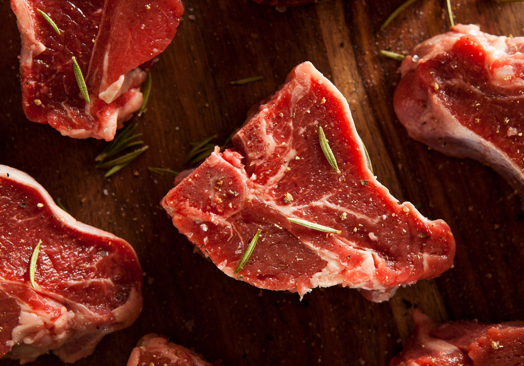 Raw Ontario lamb chops displayed on a cutting board and spiced with rosemary and black pepper. 