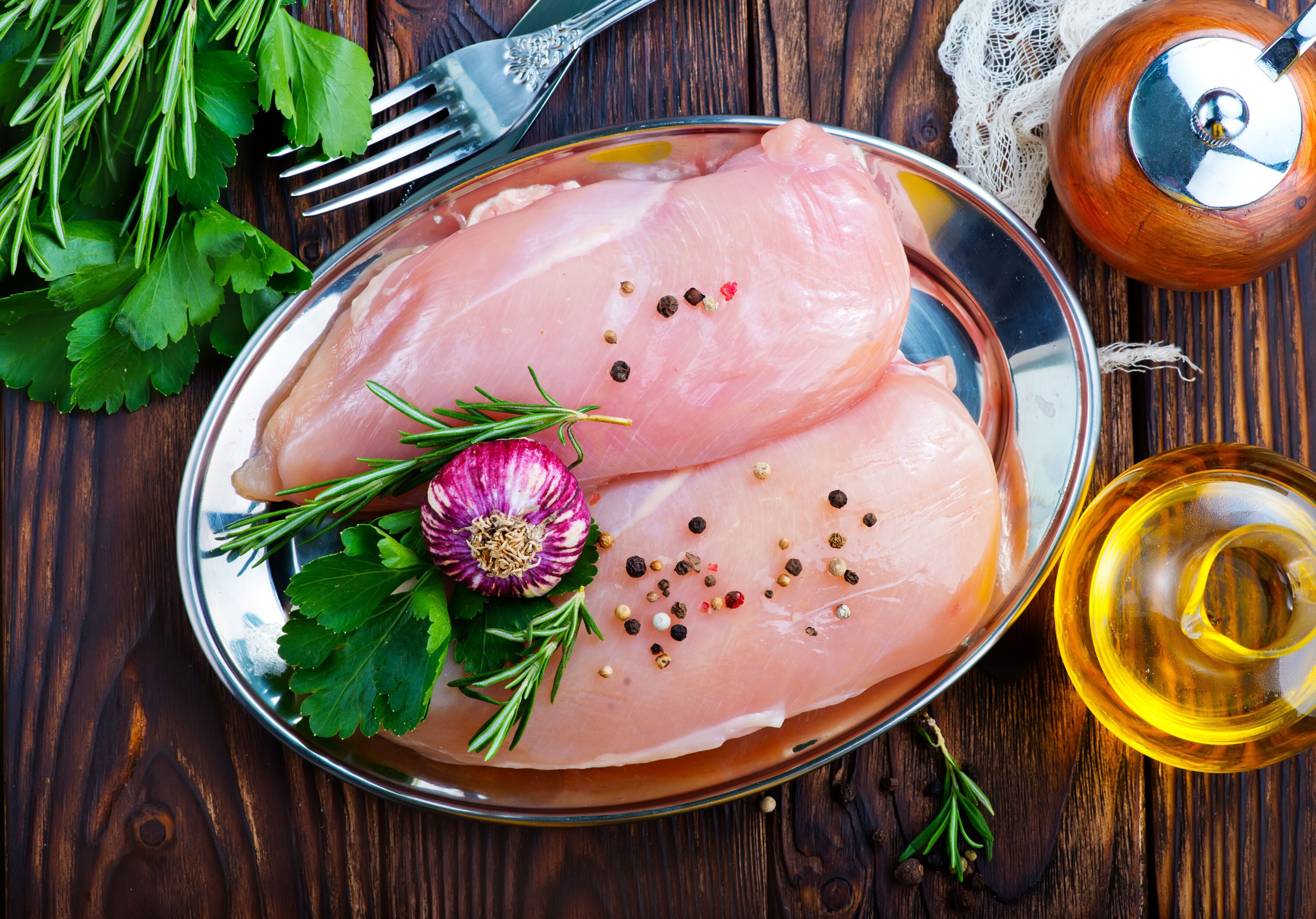 Two raw chicken breasts displayed with peppercorn, garlic, and parsley. King George's Steaks and Seafood.