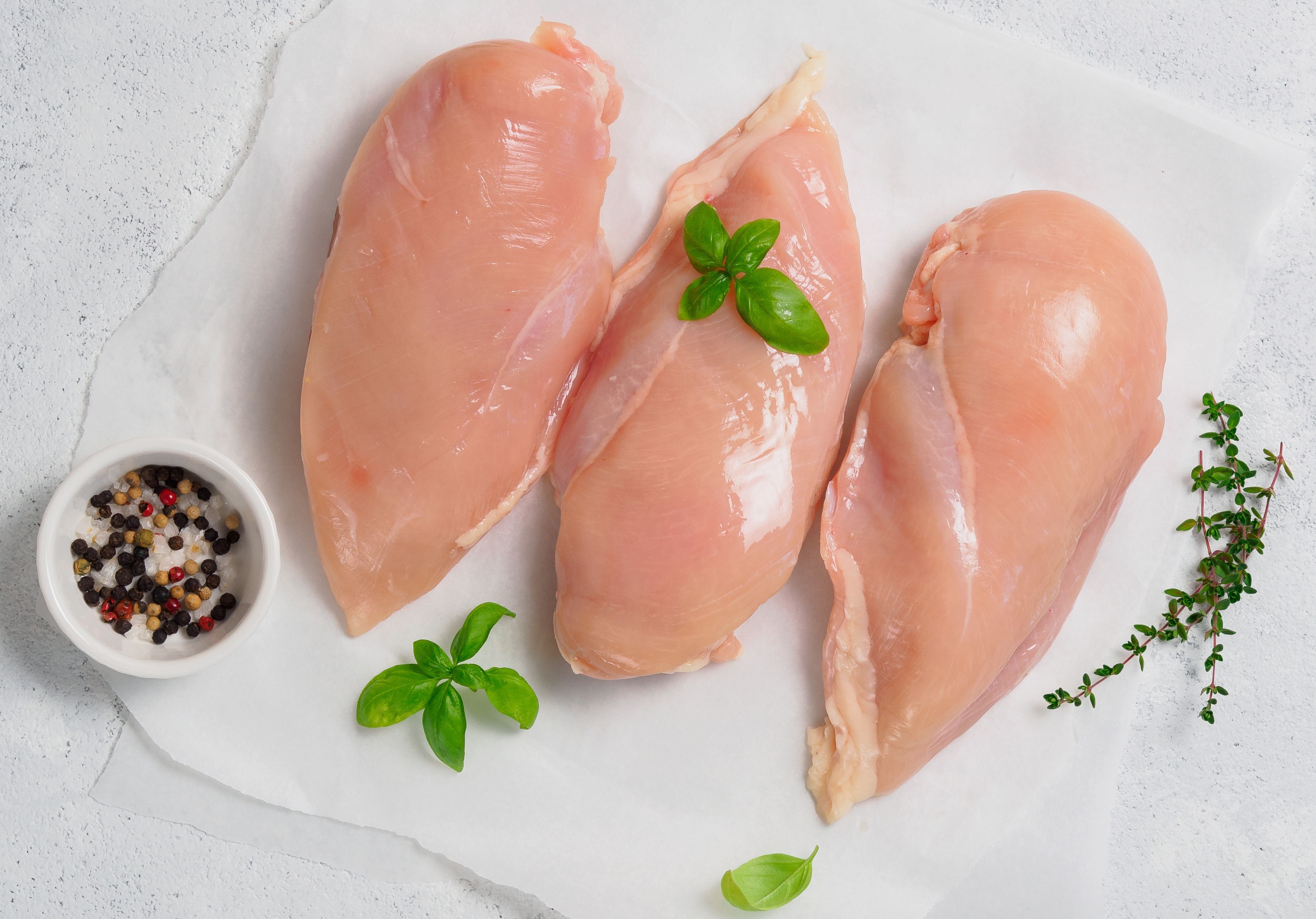 Raw organic chicken breasts displayed with sea salt, peppercorns, and fresh basil leaves. King George's Steaks and Seafood.