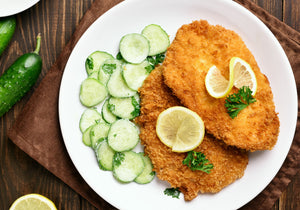 Pork schnitzel baked and served with cucumber salad, garnished with lemon wheels and parsley. King George's Steaks and Seafood.