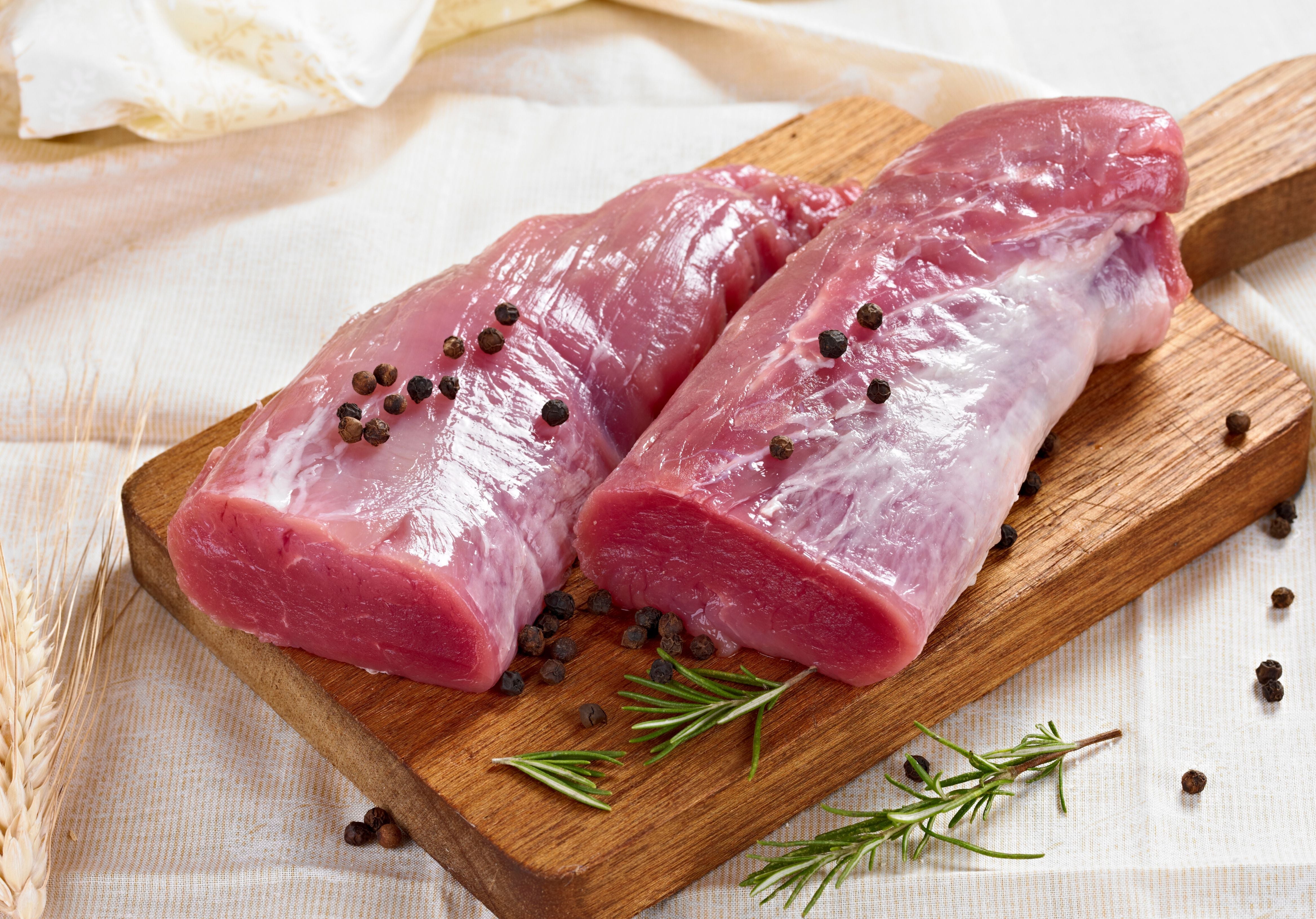 Two raw pork tenderloins displayed on top of a wooden cutting board and displayed with peppercorn and rosemary. King George's Steaks and Seafood.