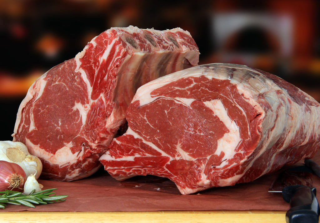 Two raw Prime Rib Roasts displayed on top of a cutting board with rosemary, shallots and garlic. King George's Steaks and Seafood.