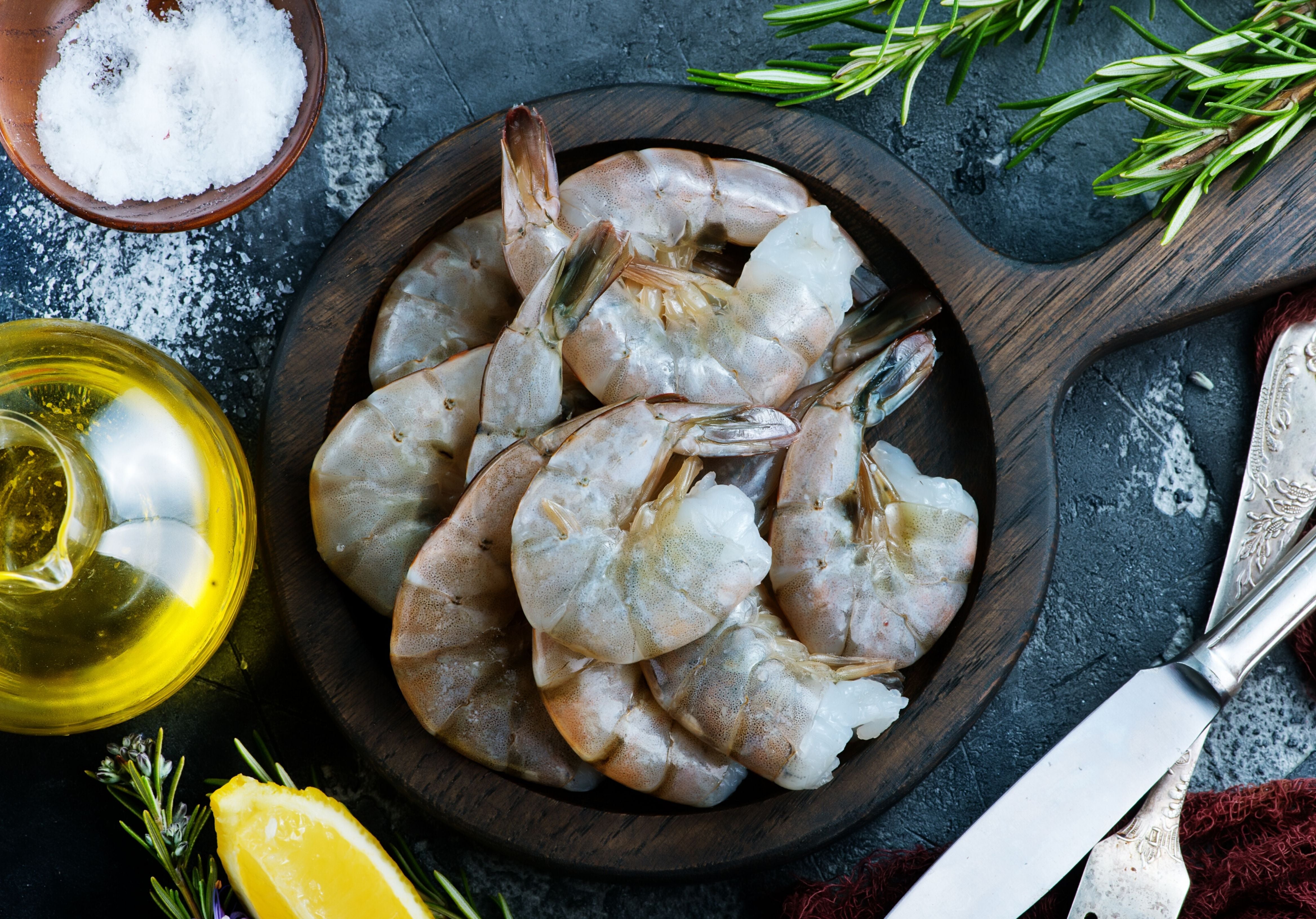 Raw shrimp in wooden pan displayed with olive oil, sea salt, rosemary and lemon. King George's Steaks and Seafood.