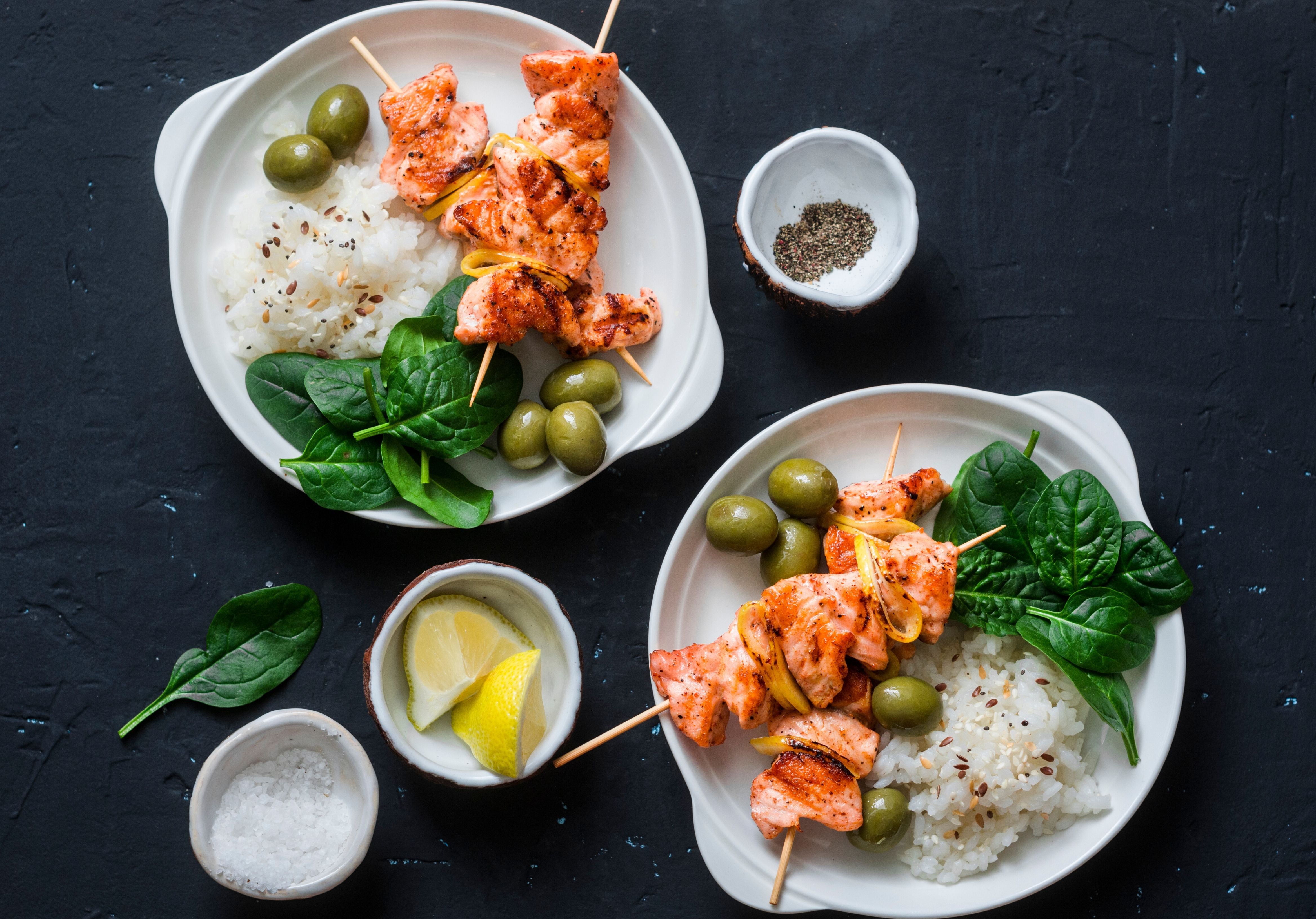 Salmon Skewers displayed on dishes accompanied with white rice and spinach. Table garnished with lemon, sea salt, and peppercorn. King George's Steaks and Seafood.