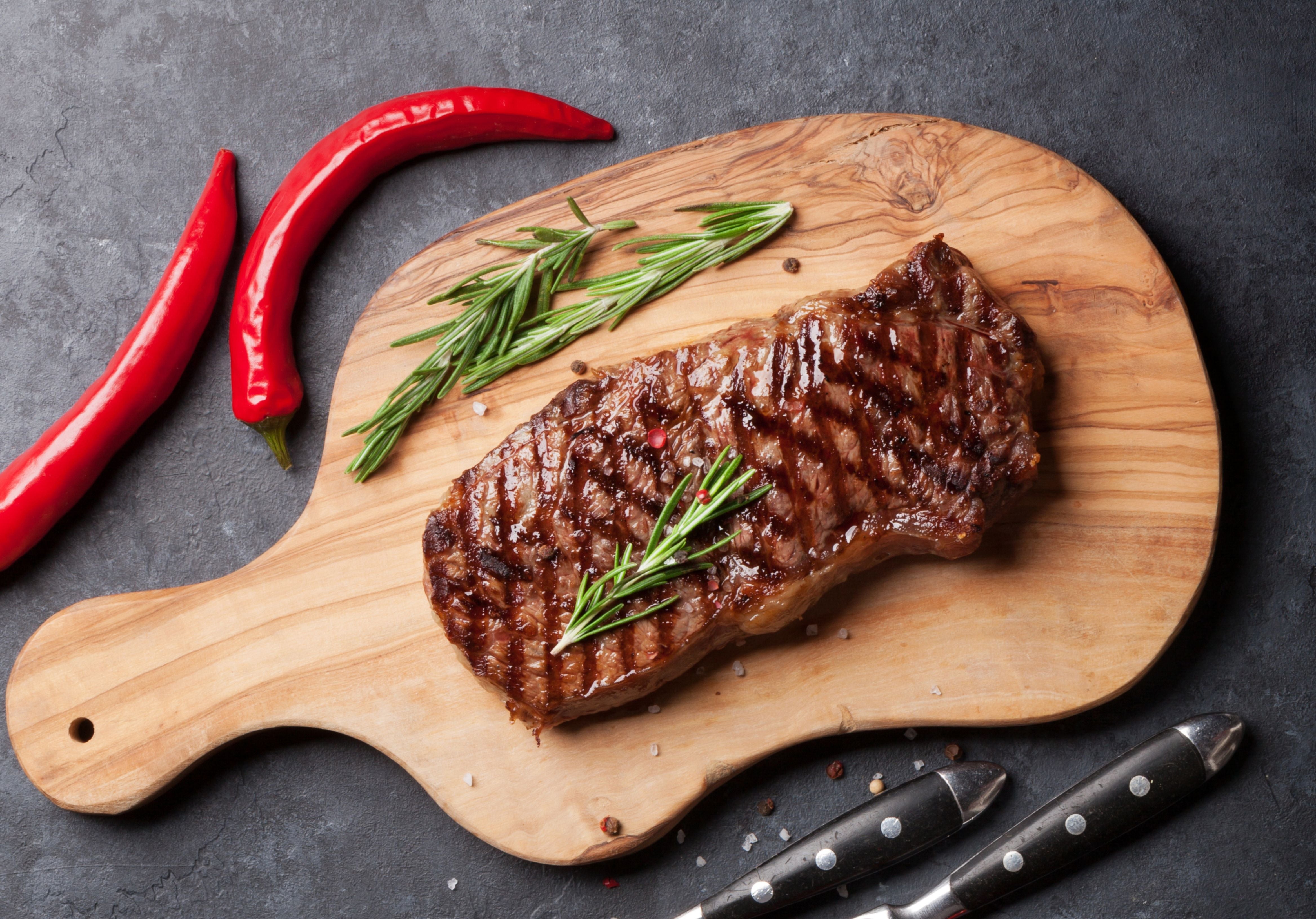 Sandwich Steak on a cutting board displayed with rosemary, red chili peppers. King George's Steaks and Seafood.