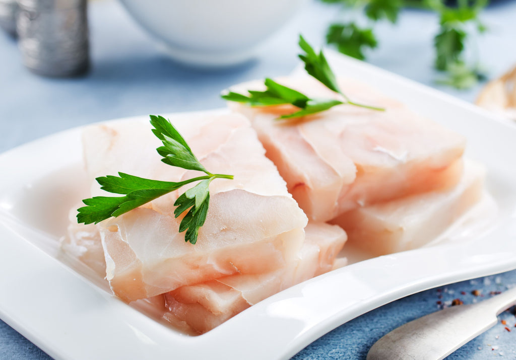 Raw Sea Bass fillets on a white plate and displayed with parsley. King George's Steaks and Seafood.