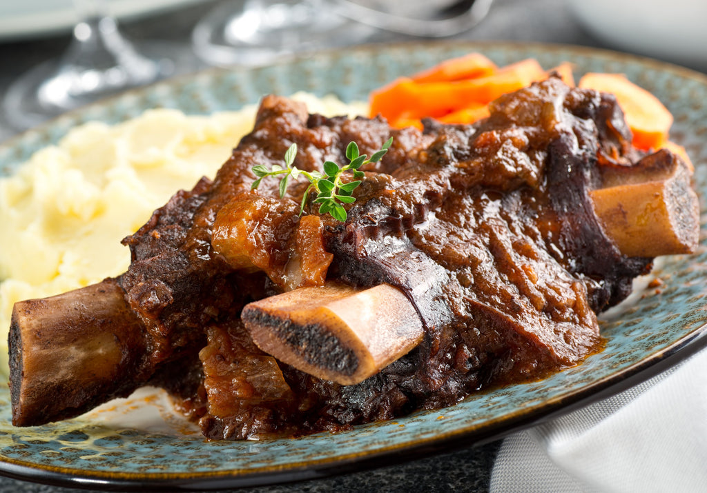 Cooked Short Ribs served on a plate with veggies and garnished with fresh leaves. King George's Steaks and Seafood.