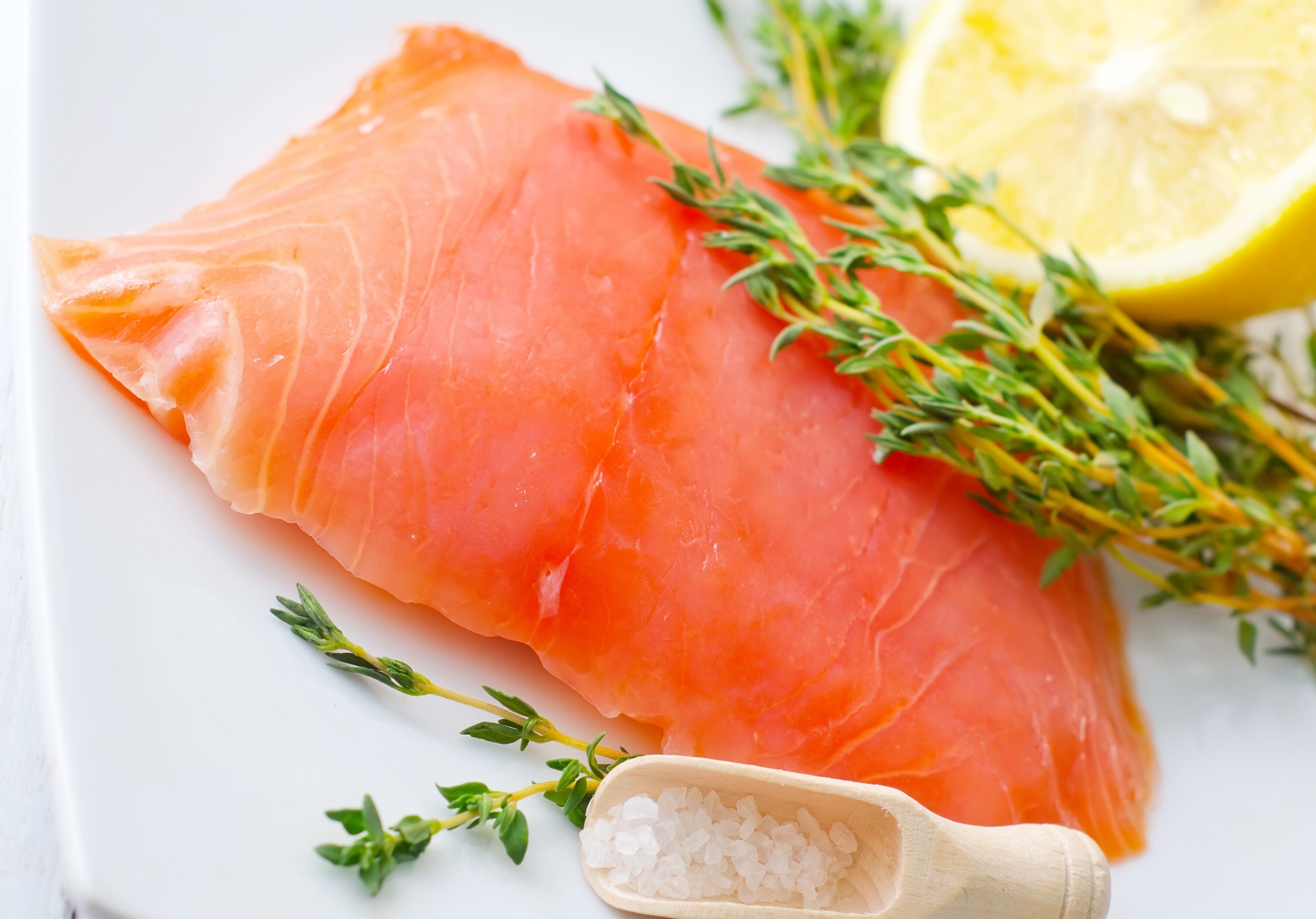 Raw Smoked Salmon displayed with sea salt, lemon, and fresh leaves. King George's Steaks and Seafood.