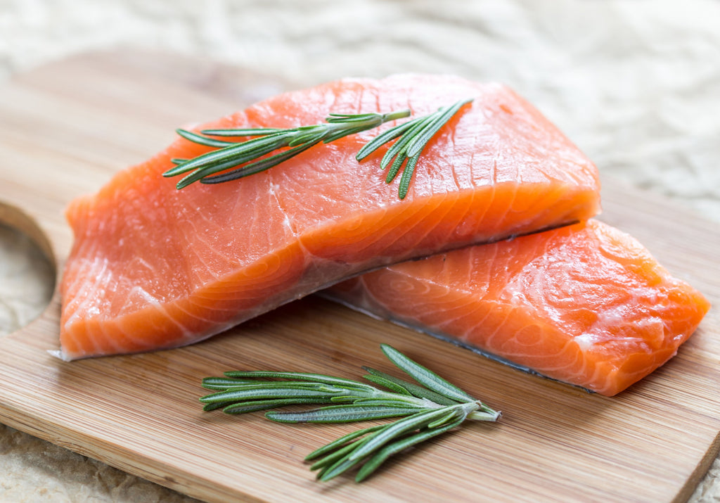 Raw Sushi Grade Salmon displayed on top of a wooden cutting board, garnished with fresh rosemary. King George's Steak and Seafood. 