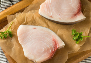 Raw Swordfish steaks with skin on displayed on a wooden cutting board. King George's Steak and Seafood.