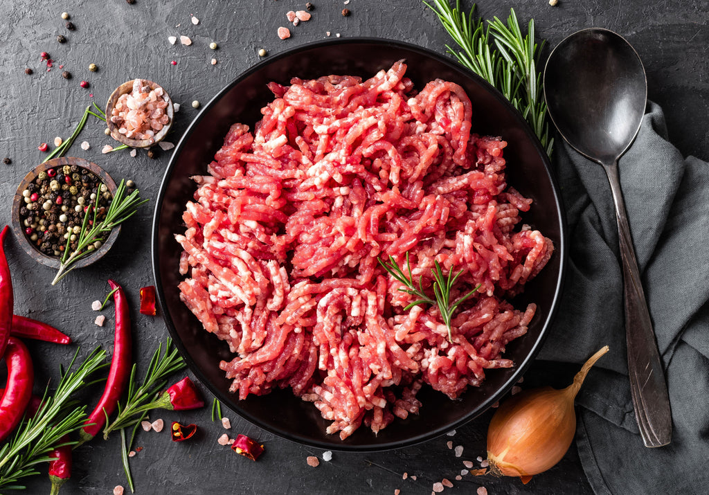 Raw Ground Beef displayed with rosemary, Himalayan salt, peppercorn, shallots, and red chilies. King George's Steak and Seafood.